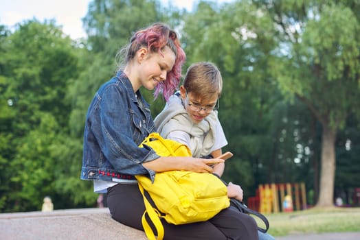 Outdoor portrait of two talking teenagers school students, boy and girl students with smartphone