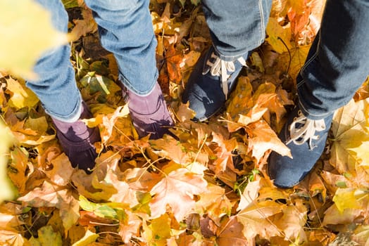 Legs in jeans and boots of woman and child on yellow leaves, leaf fall