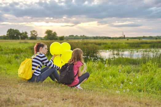 Two girls sister resting in nature, summer vacation in evening near the lake on lawn, children with soap bubbles