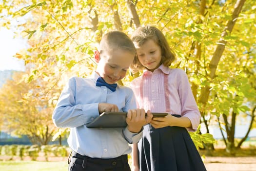 Two kids watching digital tablet, background autumn sunny park, golden hour