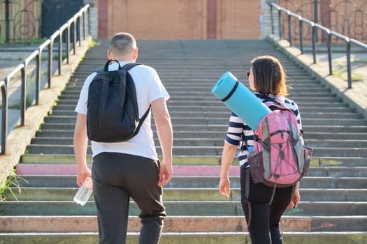 Mature couple in city on stairs, middle-aged man and woman in sportswear talking walking, back view. Active sports healthy lifestyle of age people