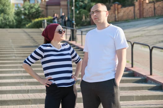 Mature couple talking near the stairs, smiling happy man and woman in casual clothes walking in the park.