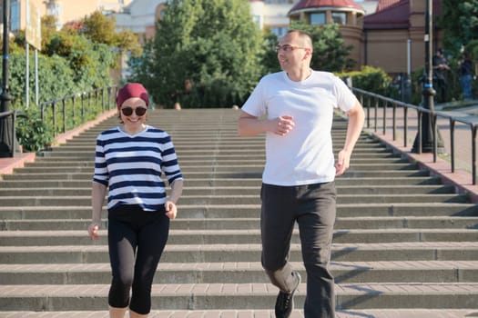 Outdoor portrait of running mature couple. Man and woman of 40 years old running up the stairs. Active sports healthy lifestyle of age people