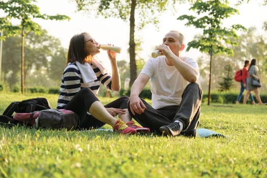 Happy mature couple sitting in the park on fitness mat, resting drinking yogurt after sports exercises. Healthy lifestyle and food age people