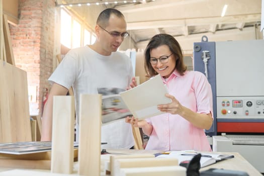 Couple man and woman designer, client, carpenter, engineer choosing wooden products, working discussion, background carpentry workshop.