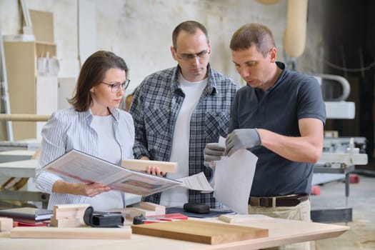 Team of woodworking workshop workers are discussing. Group of people client, designer or engineer and workers discuss work, background carpentry production