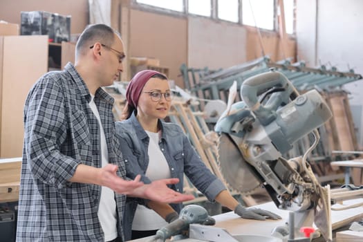 Industrial portrait of two working men and woman, talking at machine tools in workshop producing carpentry products