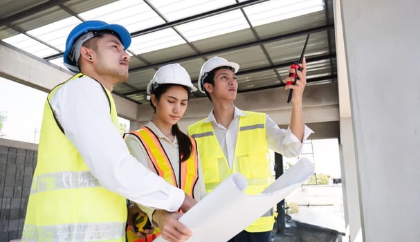 Team of professional civil engineers and architects holding project plan paper, supervising and controlling construction project work at construction site..