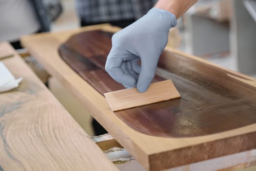 Closeup of workers hand covering wooden plank with finishing protective cover for wood, carpentry furniture woodworking production