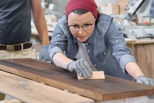 Mature craftswoman working in woodshop. Female painting wooden board with oil, varnish. Furniture joinery wood business.