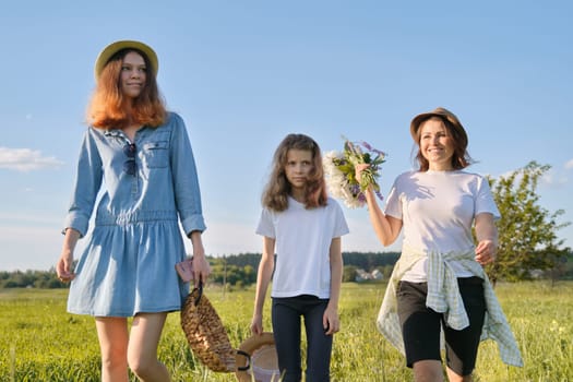 Mother with children two daughters walking along a country road, background summer meadow sunset