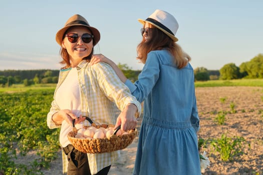 Mother and teen daughter with a basket of fresh eggs in the garden, golden hour.