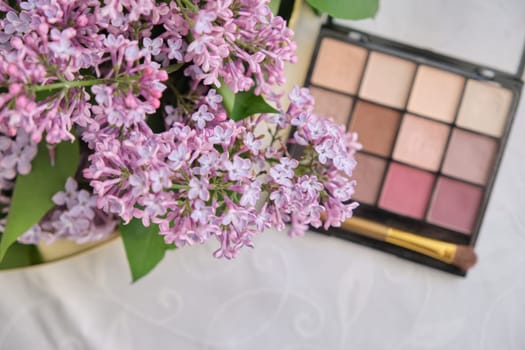 Decorative makeup cosmetics, eye shadow with brush and fresh lilac flowers close-up, top view