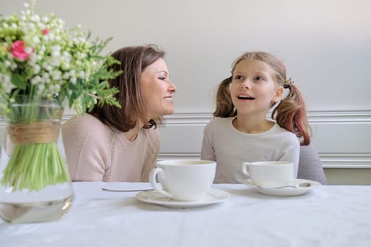 Happy smiling mother and little daughter drinking at table of cups. Parent and child having fun and talking