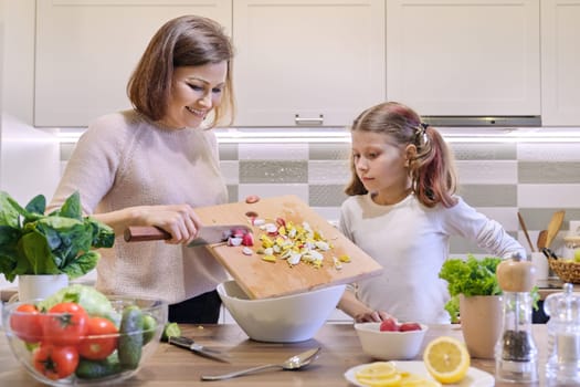 Mother and daughter cooking together in kitchen vegetable salad, parent and child are talking smiling