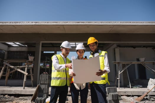 Team of professional civil engineers and architects holding project plan paper, supervising and controlling construction project work at construction site..