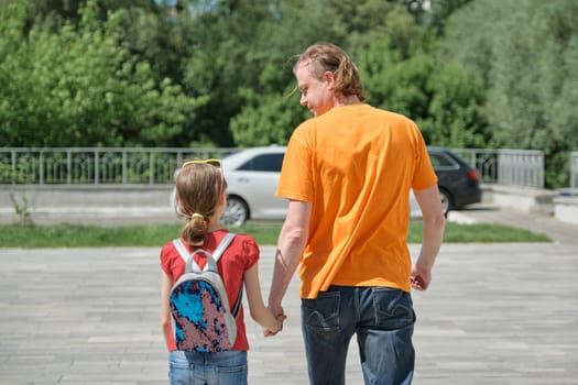 Dad walks with his daughter holding hands. Outdoor, sunny summer day, back view.