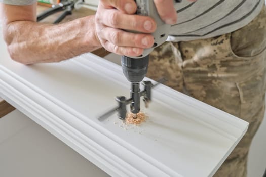 Close-up of carpenters hand using professional woodworking electric tools when working with wood. Male carving hole in wooden panel board, carpentry, woodwork, profession, people.