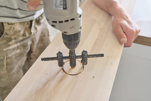 Close-up of carpenters hand using professional woodworking electric tools when working with wood. Male carving hole in wooden panel board, carpentry, woodwork, profession, people.