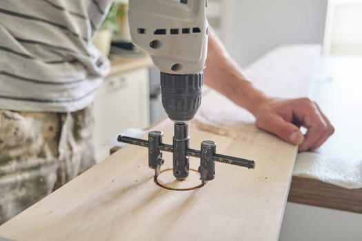 Close-up of carpenters hand using professional woodworking electric tools when working with wood. Male carving hole in wooden panel board, carpentry, woodwork, profession, people.