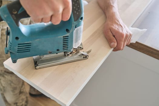 Close-up of carpenters hand using professional woodworking electric tools when working with wood. Male carving hole in wooden panel board, carpentry, woodwork, profession, people.