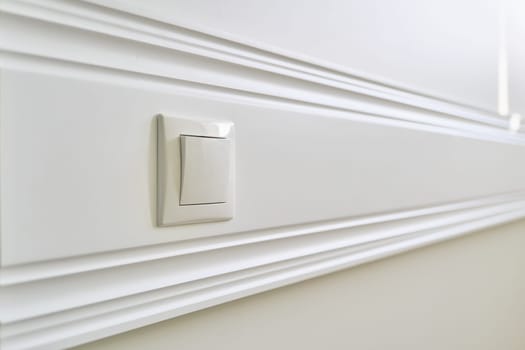 Wooden white painted panel board glued to the wall with power socket in interior close-up.