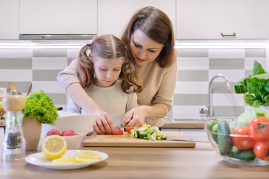Cooking healthy home meal by family. Mother and daughter cut vegetables at home in the kitchen for salad. Woman teaching child cutting tomatoes