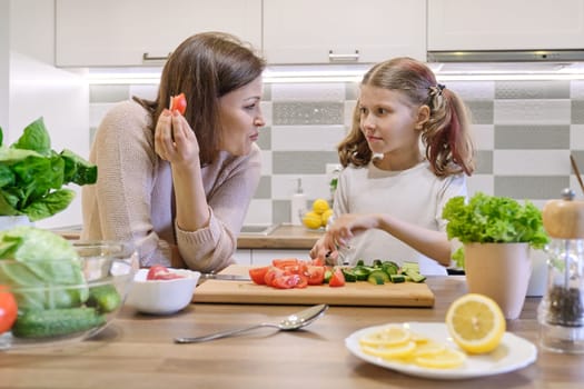 Mother and daughter cooking together in kitchen vegetable salad, parent and child are talking smiling