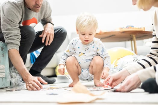 Parents playing games with child. Little toddler doing puzzle. Infant baby boy learns to solve problems and develops cognitive skills. Child development concept.