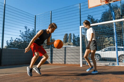 Streetball basketball game with two players, teenagers girl and boy with ball, outdoor city basketball court