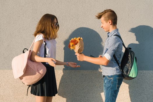 Boy gives girl bouquet of flowers. Outdoor portrait of couple teenagers.