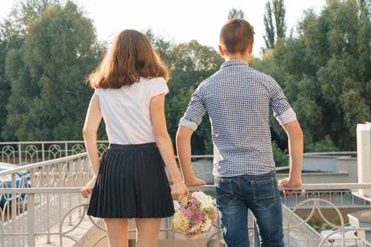 Teen youth couple boy and girl standing back, summer sunny day, girl holding bouquet of flowers in hand.