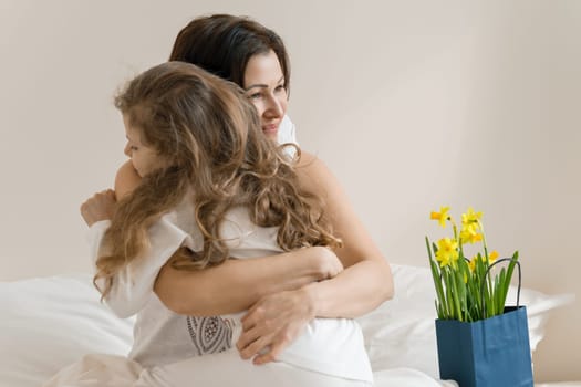 Mothers Day. Morning, mom and child in bed, mother hugging her little daughter. Background interior of bedroom, bouquet of flowers