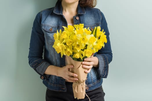 Bouquet of yellow flowers in hands of woman close-up, spring flowers daffodils, pastel green mint wall background