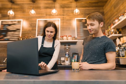 Team of coffee shop workers working near the counter with laptop computer and making coffee, cafe business.