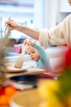 Mother and little toddler baby boy making pancakes for breakfast together in domestic kitchen. Family, lifestyle, domestic life, food, healthy eating and people concept