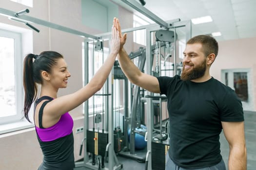 Young smiling fitness woman giving high-five to personal trainer. Fitness, sport, training, people, healthy lifestyle concept.