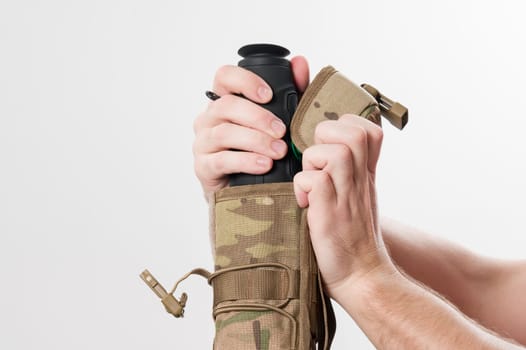 Military monocular in a case for storage and carrying, a man demonstrates a monocular in a protective case to a bag in pixels.