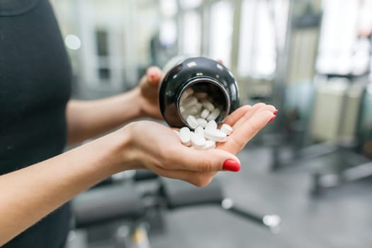 Closeup of fitness woman hands showing sports and fitness supplements, capsules, pills, gym background. Healthy lifestyle, medicine, nutritional supplements and people concept.