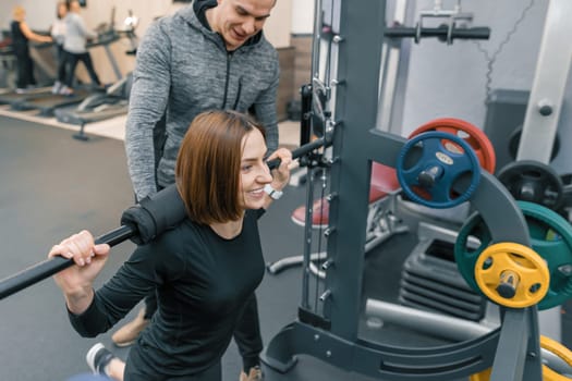 Male personal fitness trainer helping young woman to do workout in gym. Sport, athlete, training, healthy lifestyle and people concept.