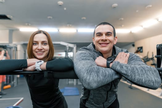 Portrait of young happy sporty couple, man and woman smiling looking into the camera, gym background.