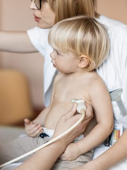 Small child being checked for heart murmur by heart ultrasound exam by cardiologist as part of regular medical checkout at pediatrician