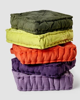 Stack of vibrant linen cushions in various colors against neutral background, showcasing home decor and comfort. Handmade furnishing accessories for cozy interior
