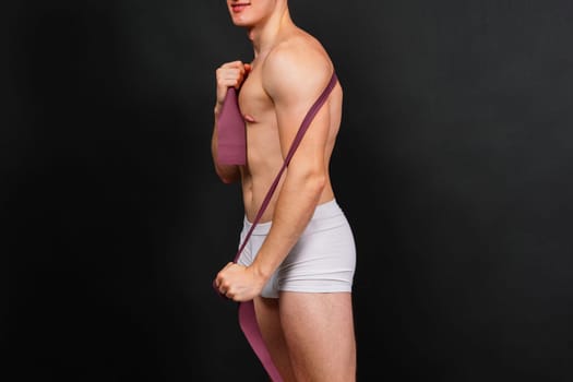 Athlete with muscular body in white panties is doing physical exercises with rubber