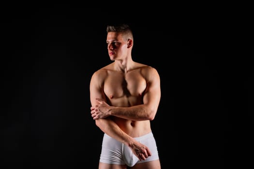 Athlete with muscular body in white panties is doing physical exercises with rubber