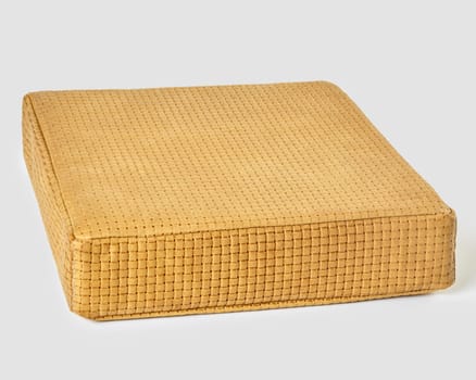 Stylish comfortable handcrafted yellow woven leather square floor cushion against neutral background. Concept of premium-class furniture accessories for modern design