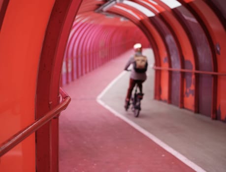 An Out Of Focus Commuter Cycling To Work Through A Pedestrian Overpass Or Walkway