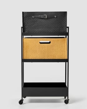 Elegant black braided leather and tan woven suede storage bins with cut-out and applied handles, placed on shelves in metal office trolley. Stylish interior accessories for organizing space