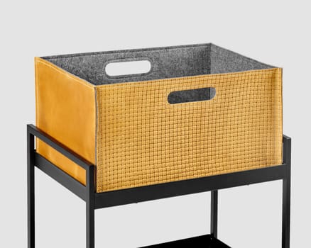 Comfortable tan suede woven box with convenient slotted handles for storing office supplies and document placed on metal shelving rack. Stylish craft accessory for interior design