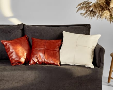 High-end brown and cream leather pillows arranged on modern dark grey sofa in chic interior of living room